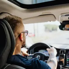 Mężczyzna w okularach przeciwsłonecznych prowadzi samochód, zastanawiając się, ile zarabia kierowca Ubera.